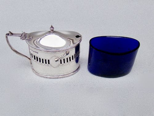 fig 2. An oval Edwardian sterling silver mustard pot featuring pierced geometric fretwork, an engraved cartouche, a hinged dome lid with a finial, and a side handle.