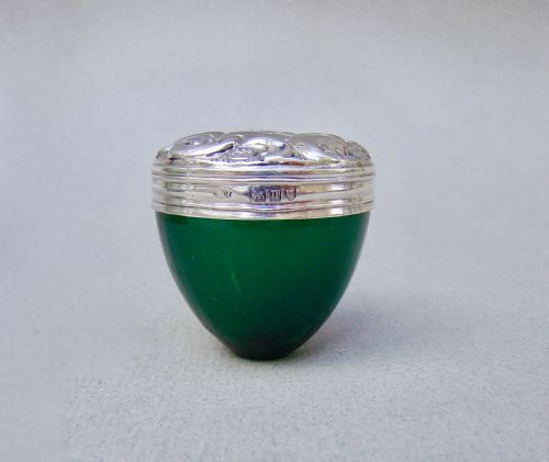 fig 1. An Edwardian sterling silver pill box with a repousse lid resting on a rounded dark green glass base.