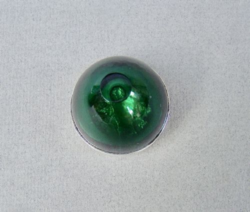 fig 2. An Edwardian sterling silver pill box with a repousse lid resting on a rounded dark green glass base.