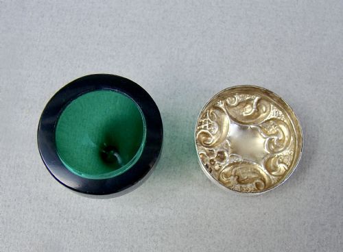 fig 3. An Edwardian sterling silver pill box with a repousse lid resting on a rounded dark green glass base.