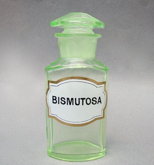 fig 2. A light-green translucent uranium glass apothecary jar featuring a fitted faceted stopper and a printed label reading Bismutosa.