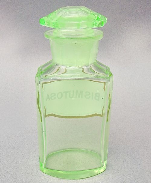 fig 1. A light-green translucent uranium glass apothecary jar featuring a fitted faceted stopper and a printed label reading Bismutosa.