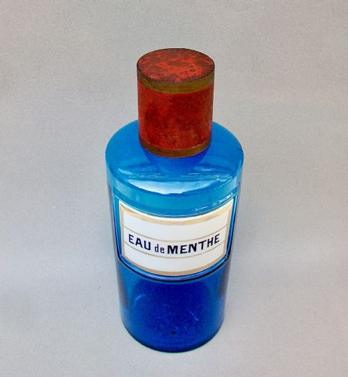 fig 1. A cylindrical turquoise blue glass apothecary jar featuring a white and gold enamel label reading Eau de Menthe and fitted with a brass and cork stopper.