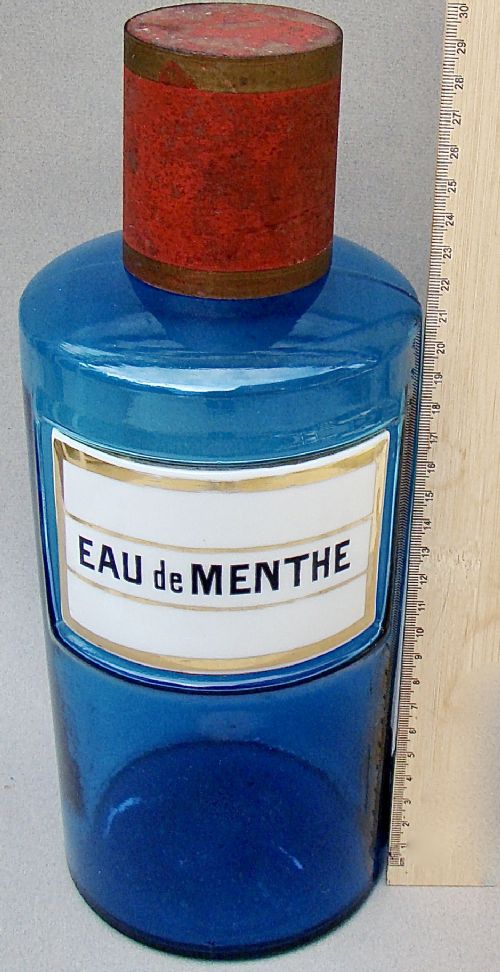 fig 2. A cylindrical turquoise blue glass apothecary jar featuring a white and gold enamel label reading Eau de Menthe and fitted with a brass and cork stopper.