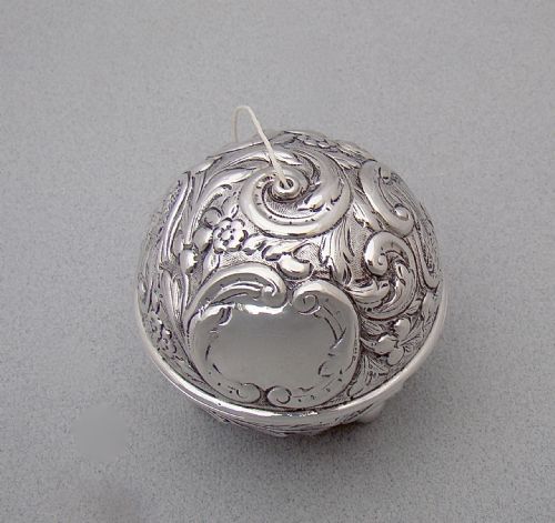 fig 1. A spherical late Victorian sterling silver string box with chased floral and scroll ornamentation, resting on three ball feet with string extending from the top opening.