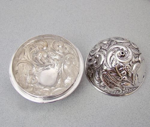 fig 3. A spherical late Victorian sterling silver string box with chased floral and scroll ornamentation, resting on three ball feet with string extending from the top opening.