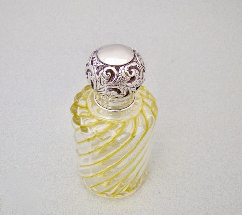 fig 1. A clear glass cologne bottle featuring diagonal yellow swirl patterns, topped with a chased sterling silver stopper.