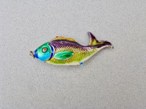 fig 1. A silver fish-shaped pendant featuring green and purple guilloche enamel across the body and a suspension loop at the mouth.