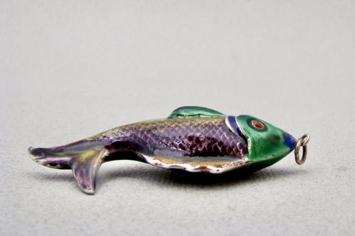 fig 2. A silver fish-shaped pendant featuring green and purple guilloche enamel across the body and a suspension loop at the mouth.