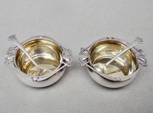 fig 1. A cased pair of Edwardian sterling silver open salt cellars with stylised handles and matching spoons set in a purple velvet fitted presentation box.
