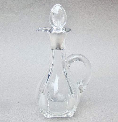 fig 1. An Art Deco clear glass oil bottle with a silver-mounted rim, stopper, and integral handle.