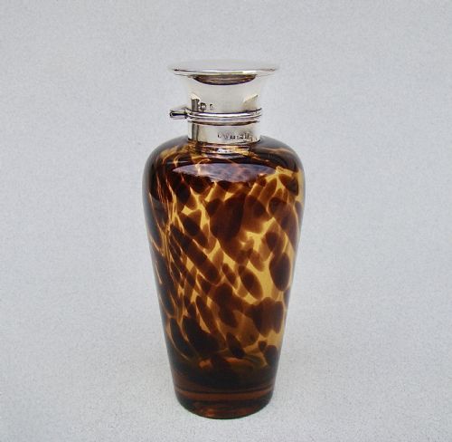 fig 1. An Edwardian silver and tortoiseshell pattern glass scent bottle featuring a polished metal cap and a mottled amber brown tapered body.