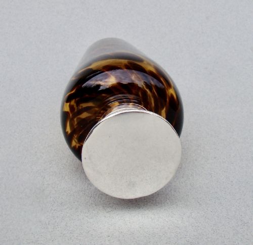 fig 2. An Edwardian silver and tortoiseshell pattern glass scent bottle featuring a polished metal cap and a mottled amber brown tapered body.