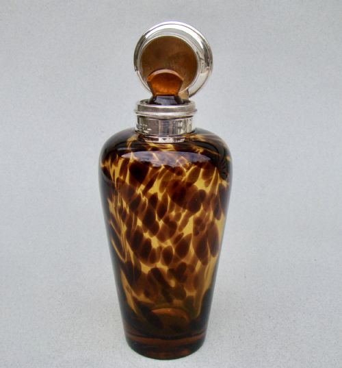 fig 3. An Edwardian silver and tortoiseshell pattern glass scent bottle featuring a polished metal cap and a mottled amber brown tapered body.