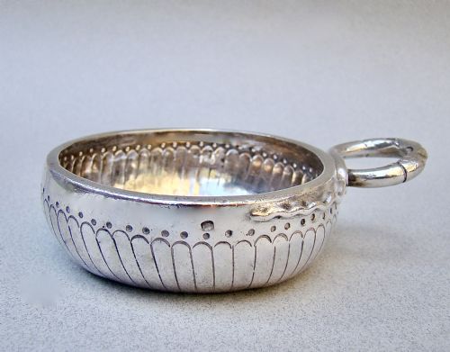 fig 1. A shallow early 19th-century French silver wine taster featuring fluted gadrooning, punchwork detailing, engraved rim lettering, and a ring handle.
