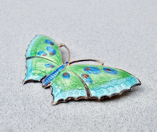 fig 1. A butterfly brooch constructed from sterling silver featuring bright green, turquoise, and blue guilloche enamel across the wings and body.