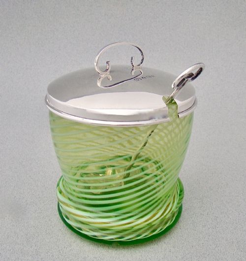 fig 2. A green spiral-patterned vaseline glass preserve pot with a polished hallmarked silver lid and matching silver spoon.