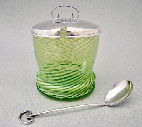 fig 1. A green spiral-patterned vaseline glass preserve pot with a polished hallmarked silver lid and matching silver spoon.