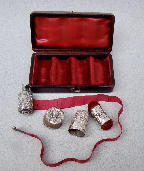 fig 1. An open dark-cased Victorian sewing set lined with crimson red silk velvet, containing four decorated silver tools including a thimble, needle case, pin cushion, and waxer.