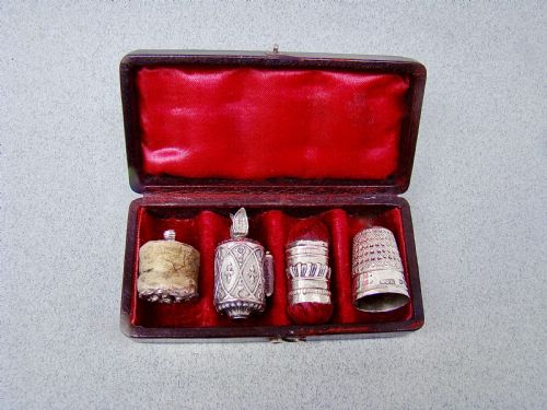 fig 2. An open dark-cased Victorian sewing set lined with crimson red silk velvet, containing four decorated silver tools including a thimble, needle case, pin cushion, and waxer.