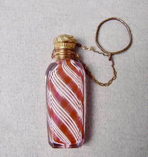 fig 1. A miniature 19th-century French Clichy clear glass scent bottle featuring internal pink and white diagonal swirls, topped with an embossed gilt brass cap and suspension ring.