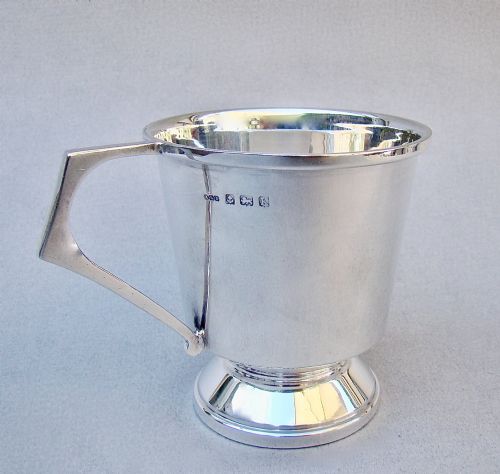fig 1. A sterling silver Art Deco christening mug with a flared body, geometric angular handle, and stepped pedestal base.
