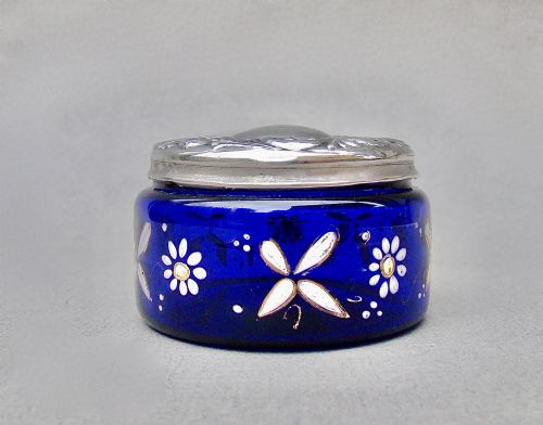 fig 1. A small cylindrical cobalt blue glass jar decorated with white enamelled floral motifs and topped with an embossed silver lid.