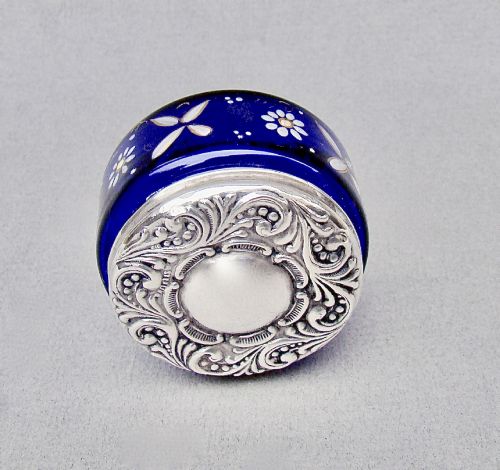 fig 2. A small cylindrical cobalt blue glass jar decorated with white enamelled floral motifs and topped with an embossed silver lid.