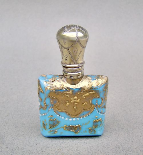 fig 1. A small rectangular turquoise glass scent bottle featuring intricate gold scrollwork, white beaded enamel, and an engraved silver-gilt cap.