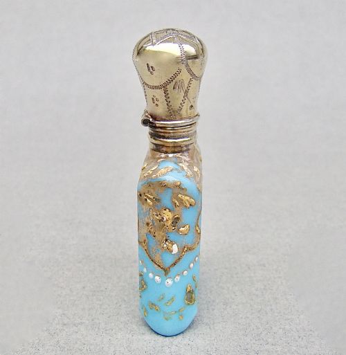 fig 2. A small rectangular turquoise glass scent bottle featuring intricate gold scrollwork, white beaded enamel, and an engraved silver-gilt cap.