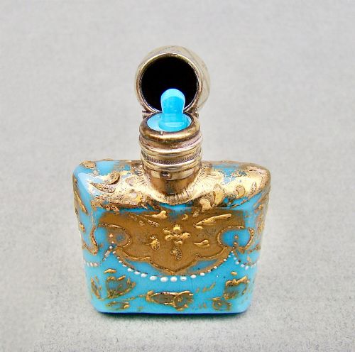 fig 3. A small rectangular turquoise glass scent bottle featuring intricate gold scrollwork, white beaded enamel, and an engraved silver-gilt cap.