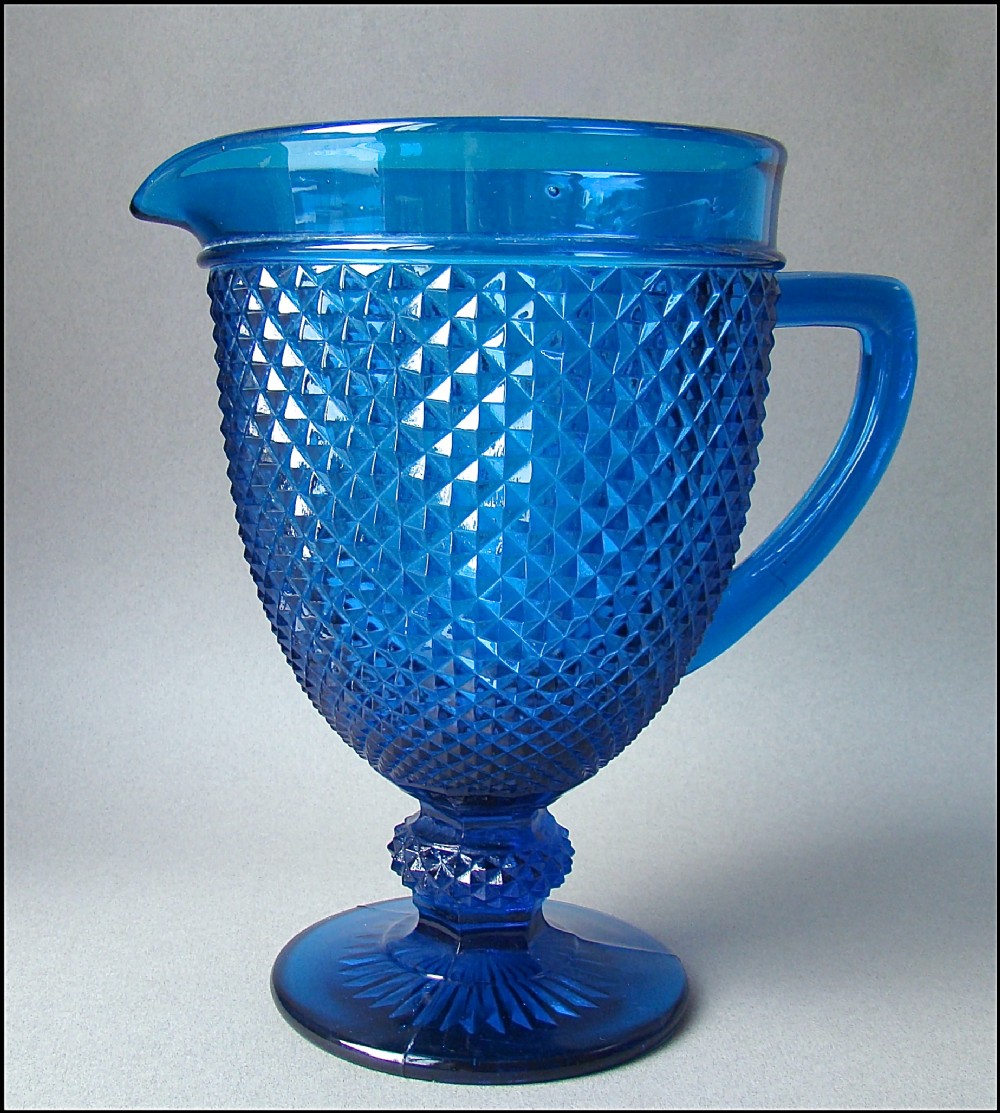 A cobalt blue Victorian pressed glass water jug featuring a diamond pattern body, moulded handle, smooth rim, and circular pedestal foot.