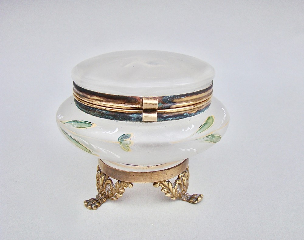A rounded frosted glass trinket box featuring painted green leaf motifs, a brass hinged rim, and four scroll-form brass feet.