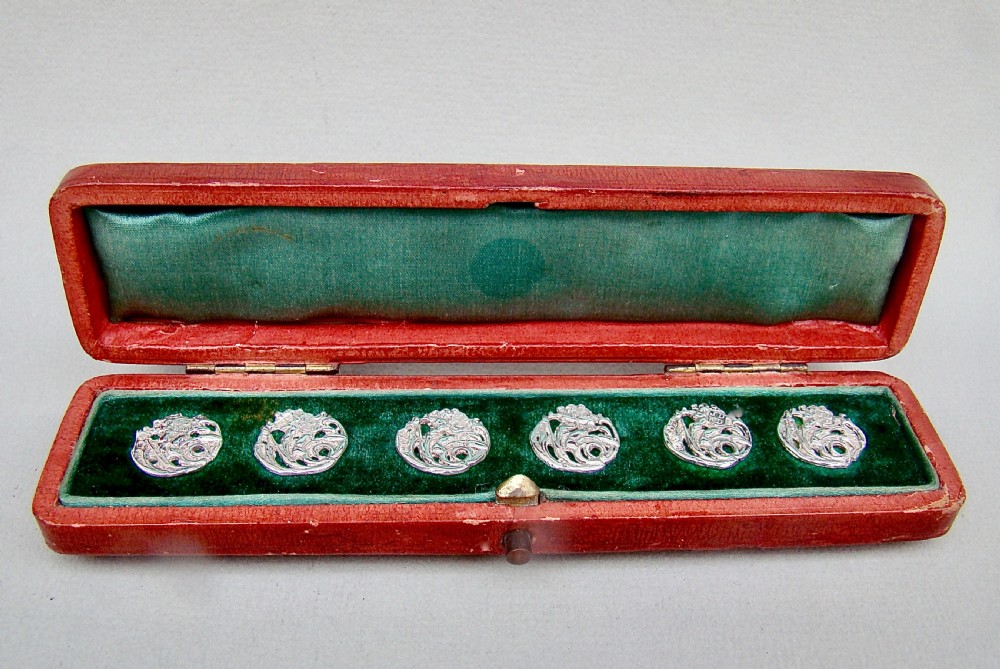 A cased set of six Art Nouveau pierced sterling silver buttons arranged inside a red velvet-lined fitted box. View II