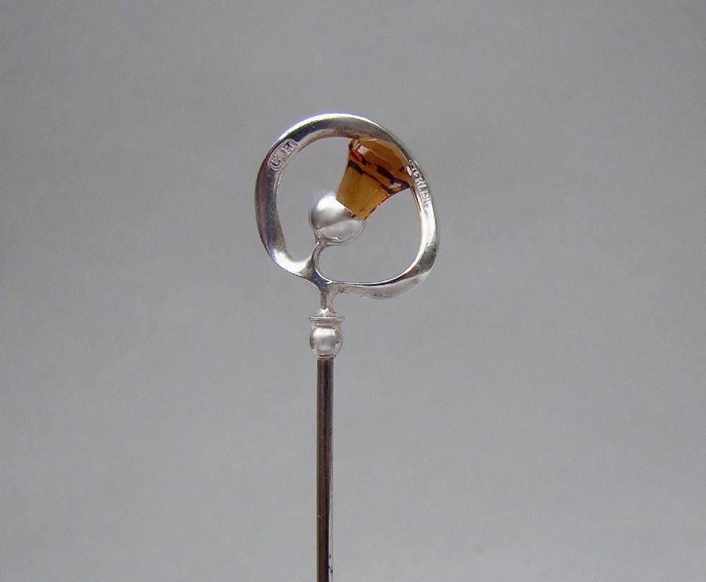 An antique silver hat pin featuring a Scottish thistle design set with an amber glass top, stamped with C.H maker marks.