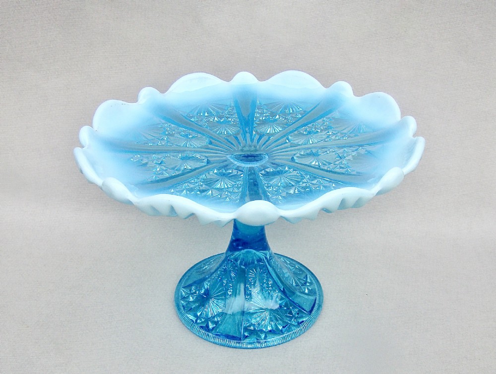 A Victorian blue pearline glass cake stand featuring a crimped opalescent edge, geometric pressed pattern, and pedestal base.