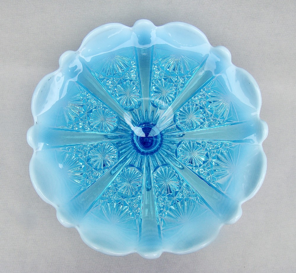 A Victorian blue pearline glass cake stand featuring a crimped opalescent edge, geometric pressed pattern, and pedestal base. View III