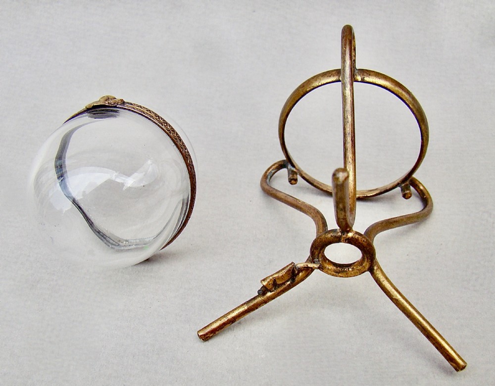 A clear egg-shaped glass casket set within a hinged gilt metal ring and supported on a three-legged tripod stand. View V