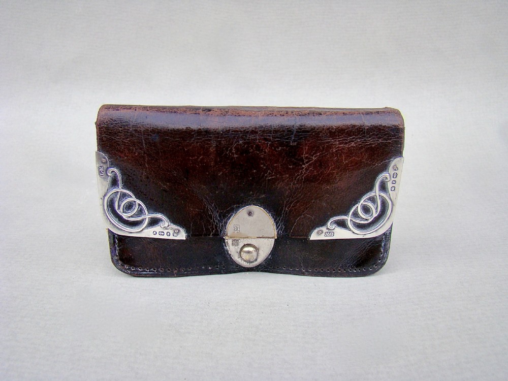 A late Victorian dark brown leather purse featuring scroll-patterned silver corner mounts with hallmarks and an oval metal central clasp.