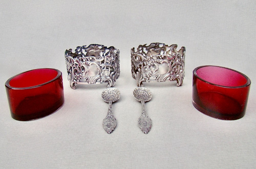 A pair of 19th-century French silver salt cellars with pierced rococo scrollwork frames, ruby glass liners, and matching silver salt spoons. View IV