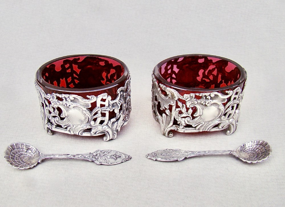 A pair of 19th-century French silver salt cellars with pierced rococo scrollwork frames, ruby glass liners, and matching silver salt spoons. View VII