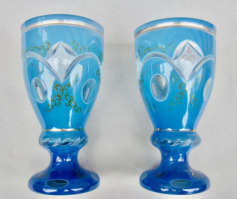 A pair of late nineteenth-century Bohemian blue cased glass goblets featuring cut-to-clear oval panels and gilt floral decoration.