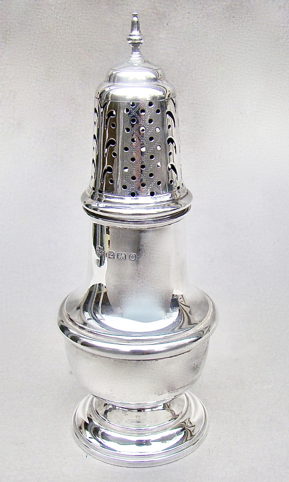 A solid silver sugar caster featuring a baluster body, hallmarks on the neck, a pierced dome lid, and a turned finial top.