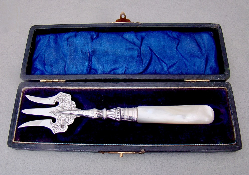 An Edwardian sterling silver three-tined bread fork with an engraved blade and mother of pearl handle inside an open fitted case.