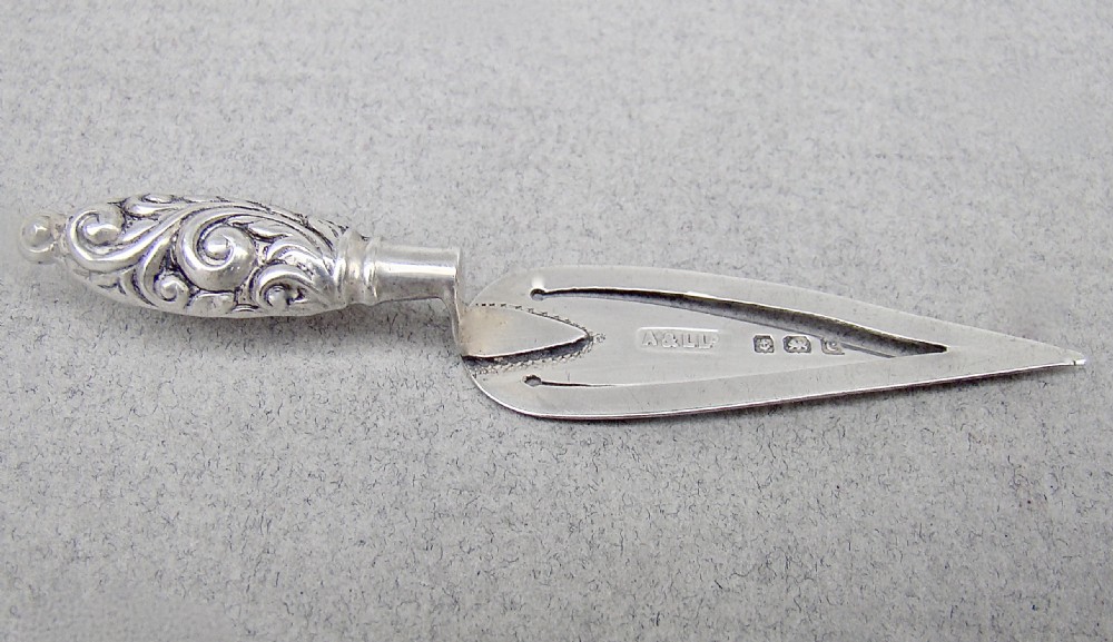 An Edwardian sterling silver bookmark shaped like a miniature trowel with an embossed scrollwork handle and British hallmarks.