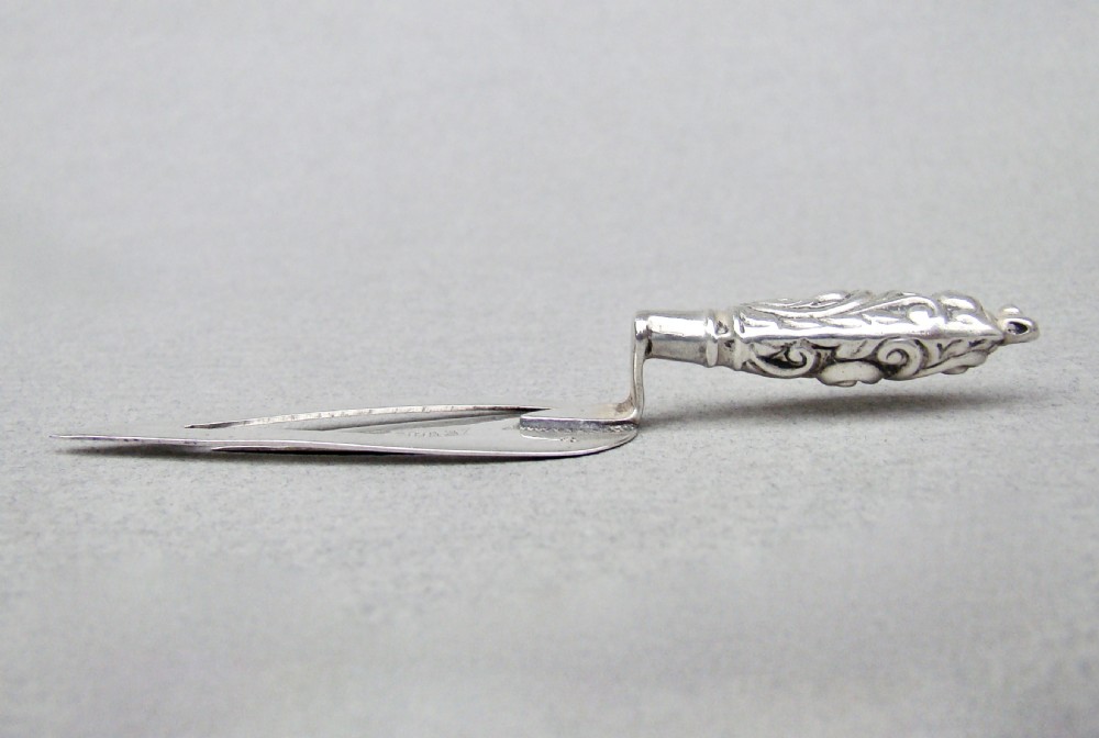 An Edwardian sterling silver bookmark shaped like a miniature trowel with an embossed scrollwork handle and British hallmarks. View IV