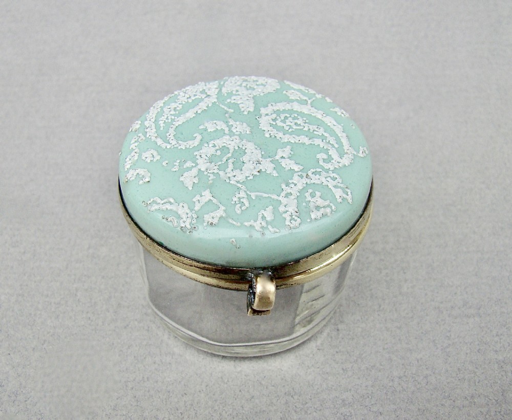 A small circular late 19th-century clear glass trinket box featuring a hinged brass mount and a pale green enamelled lid with raised white decoration.