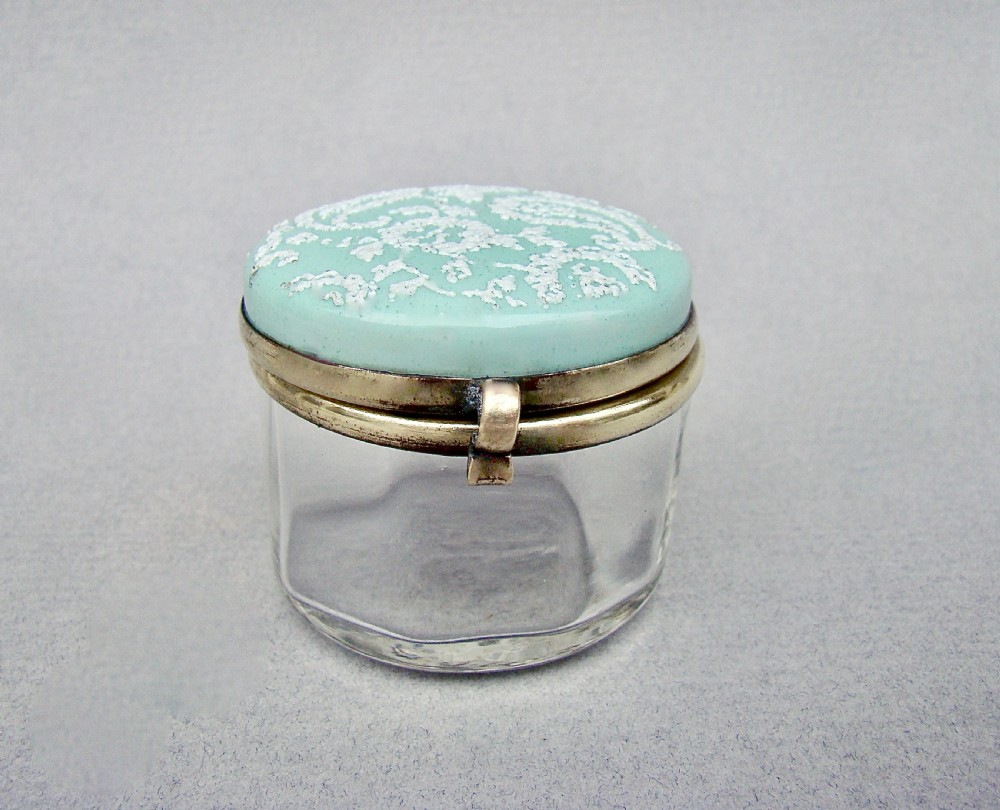 A small circular late 19th-century clear glass trinket box featuring a hinged brass mount and a pale green enamelled lid with raised white decoration. View II