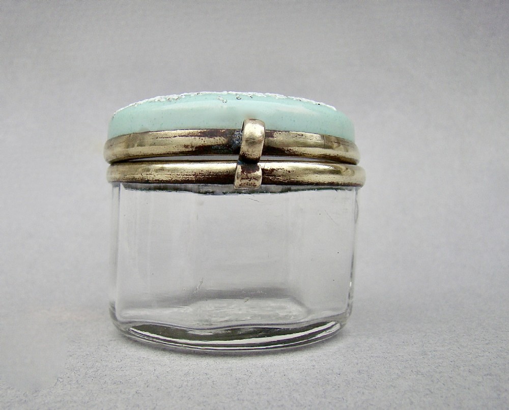 A small circular late 19th-century clear glass trinket box featuring a hinged brass mount and a pale green enamelled lid with raised white decoration. View IV