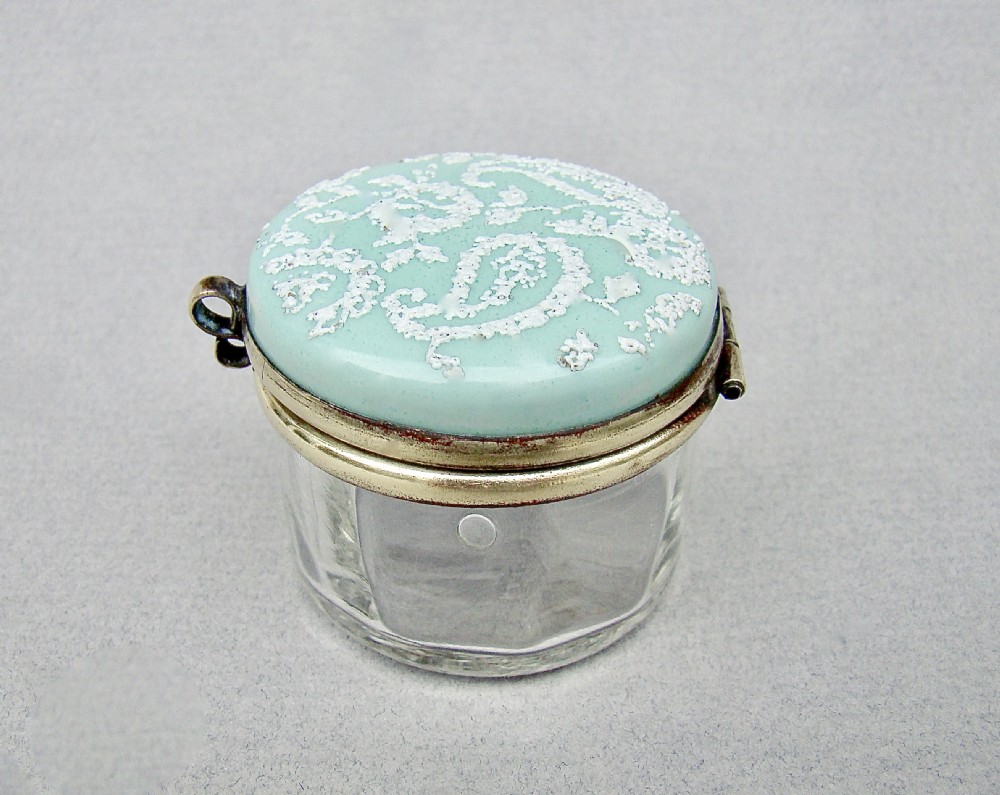 A small circular late 19th-century clear glass trinket box featuring a hinged brass mount and a pale green enamelled lid with raised white decoration. View VI